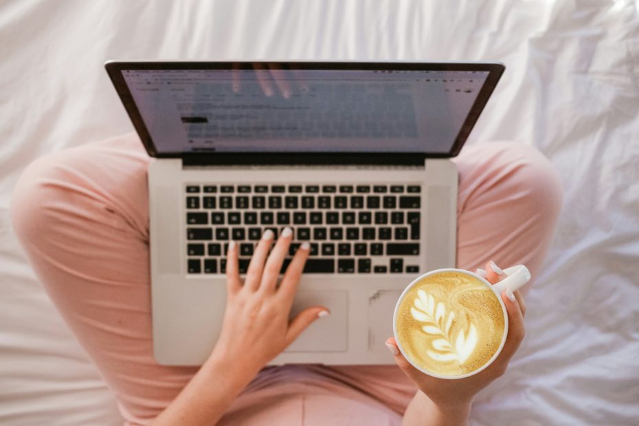 person using MacBook Pro and holding cappuccino