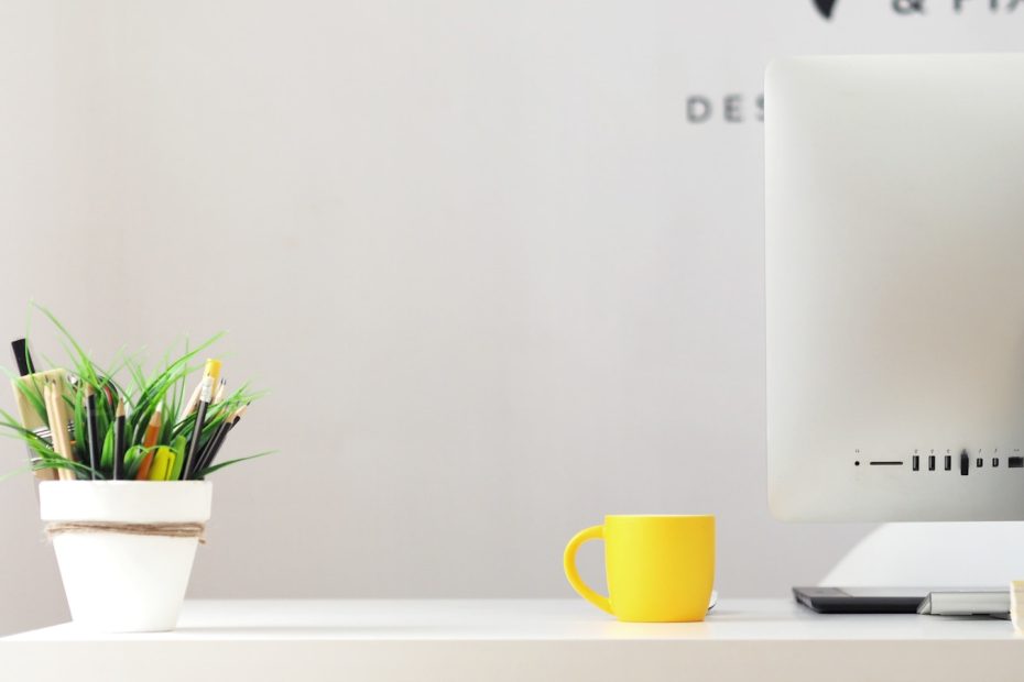 yellow ceramic mug beside gray aluminum iMac